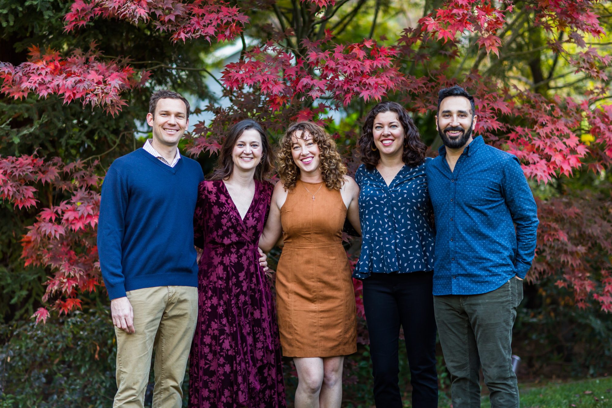 five people standing in front of autumn trees smiling