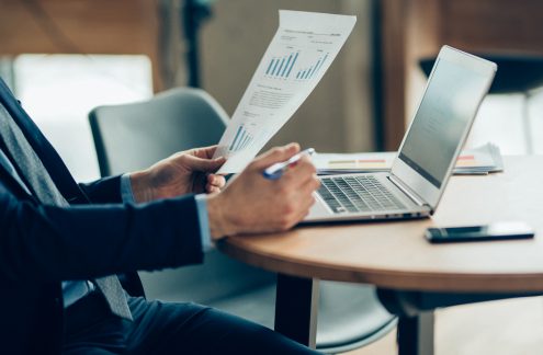 Businessman working on a laptop and reviewing paper with graphs