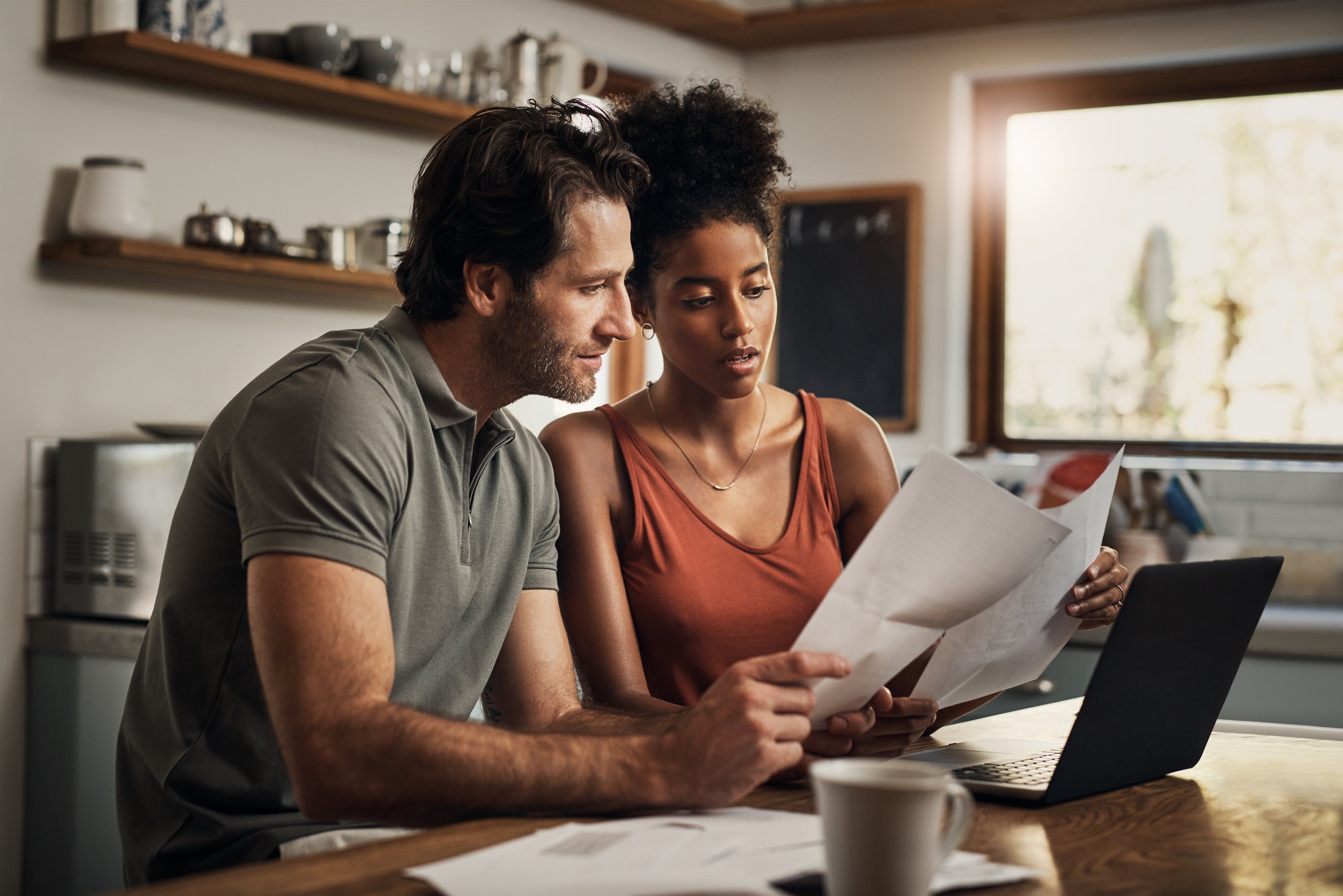 Couple-looking at paperwork in kitchen with laptop