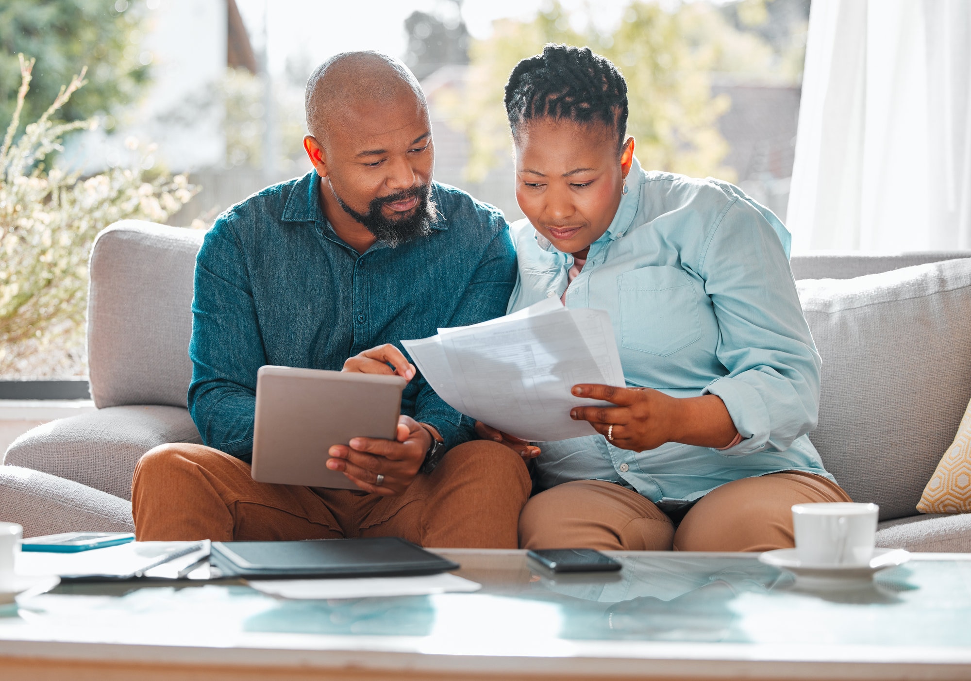 Couple using a tablet and looking through documents at home