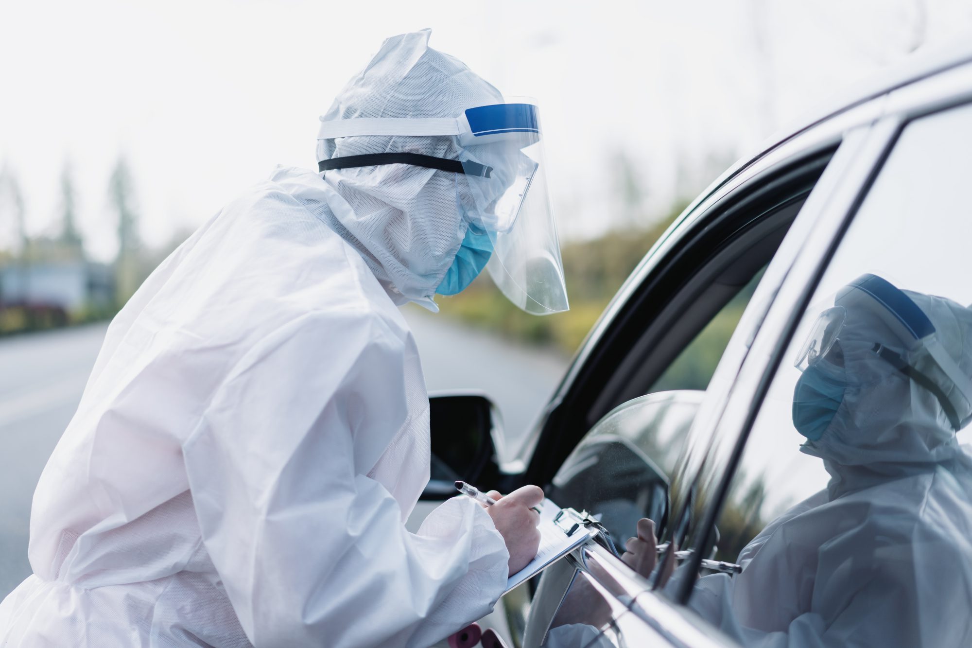 a medical worker conducts COVID-19 testing at a car window