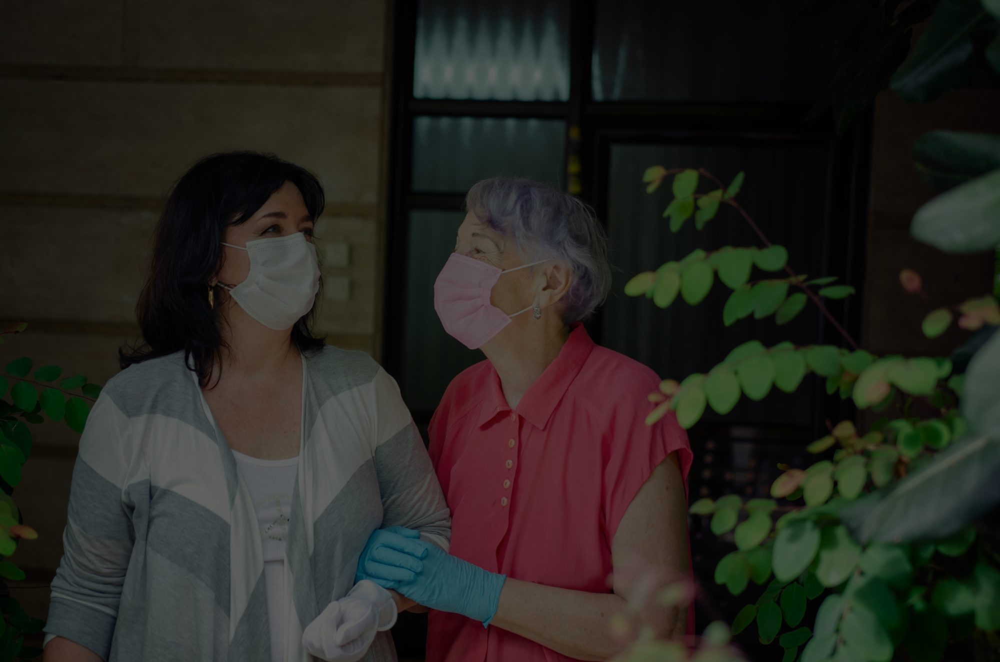 Two women with linked arms walking while wearing protective masks