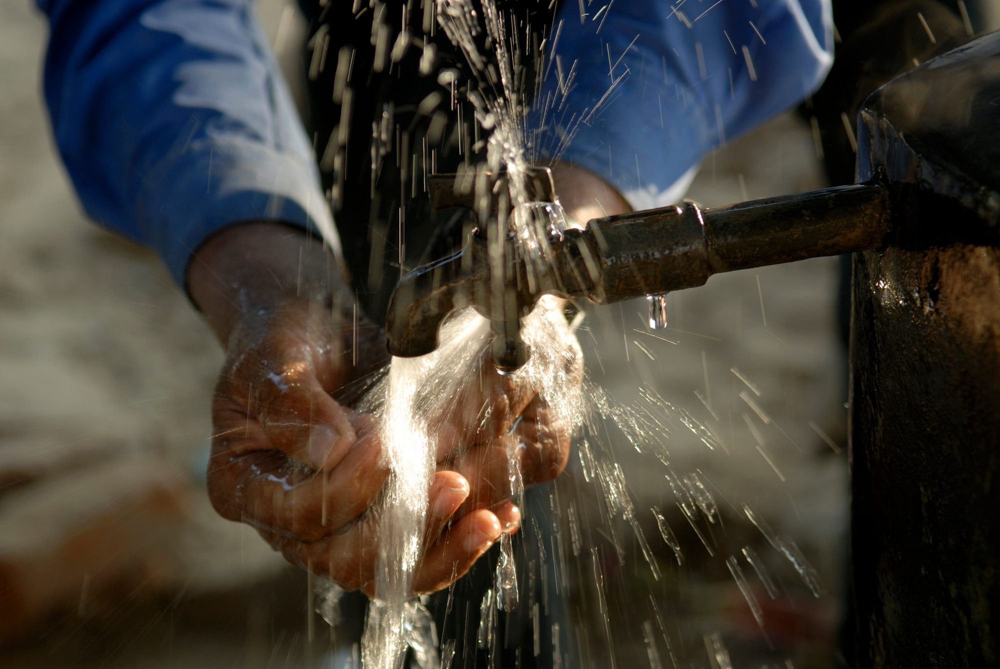 A man washing his hands at an outdoor faucet
