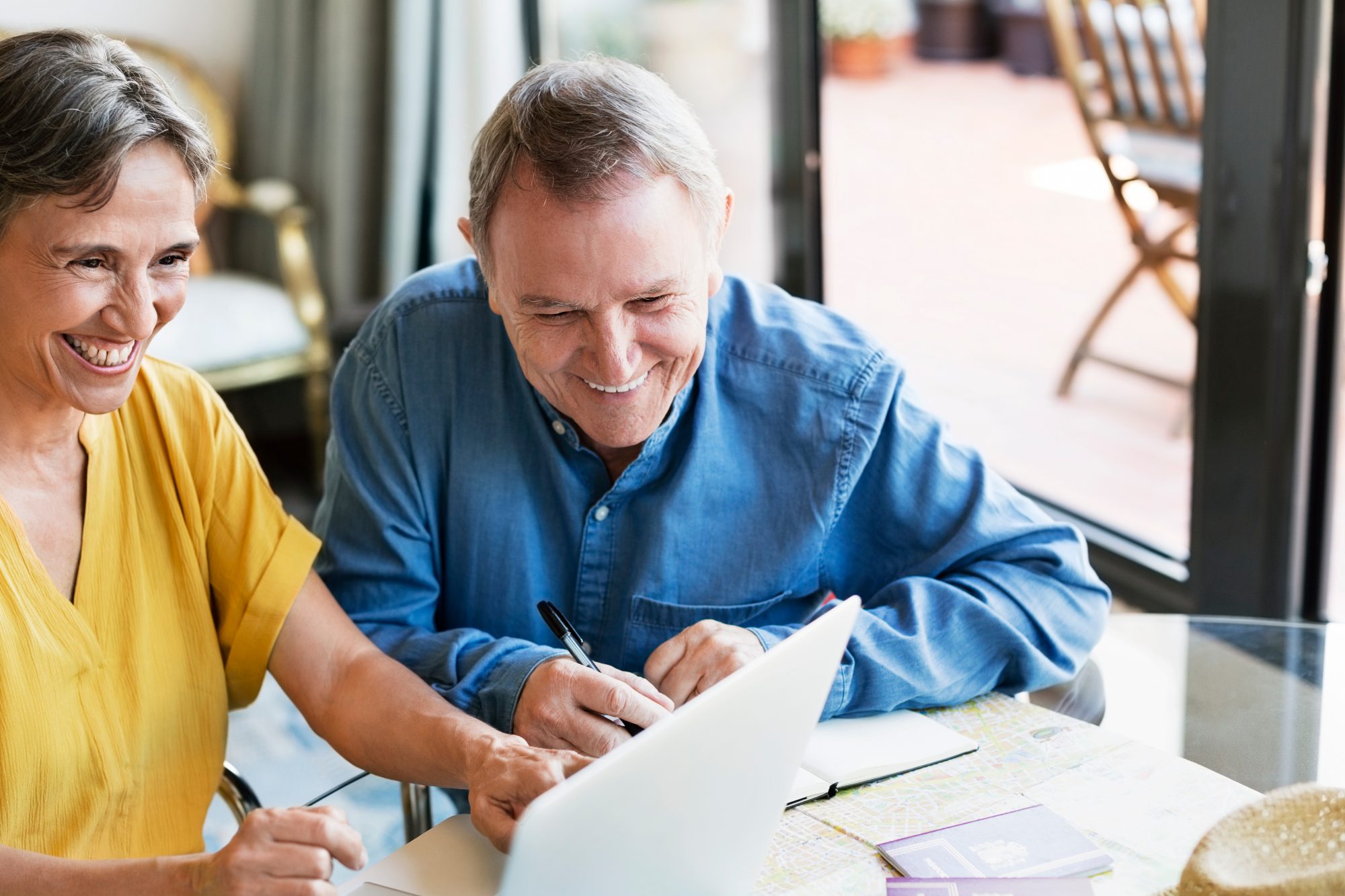 A man and woman smile as they look at their laptop and do paperwork.