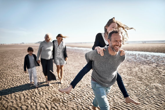 family walking on beach - dad running with child on his back