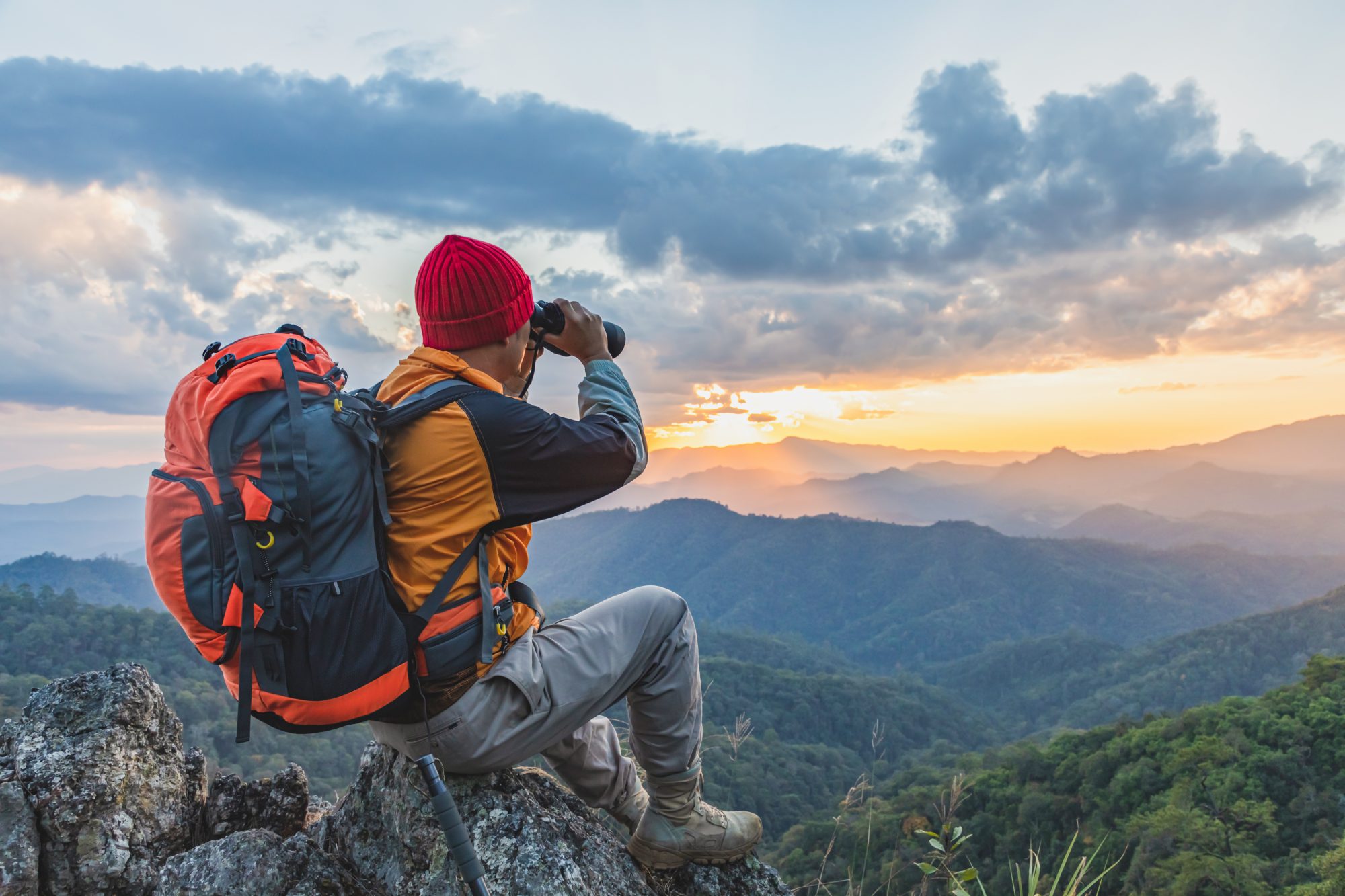 Hiker with backpack sitting on a mountain looking at the sunset