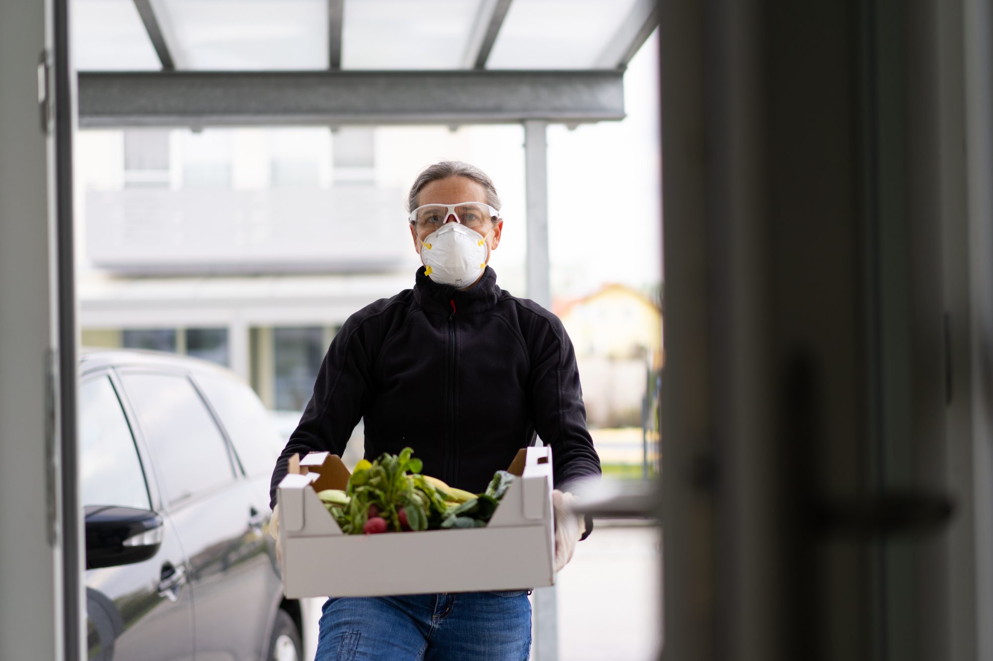 Man holding a box of vegetables with a face mask on