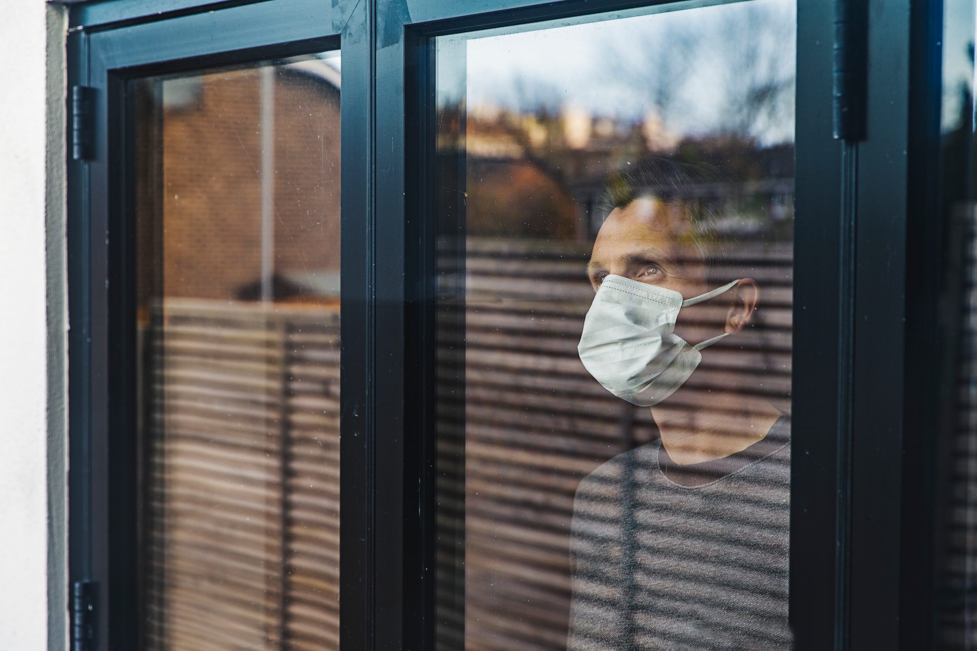 Man with a mask on his face looking out the window