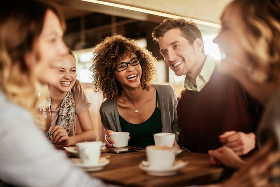 Group of young people laughting around a table drinking coffee