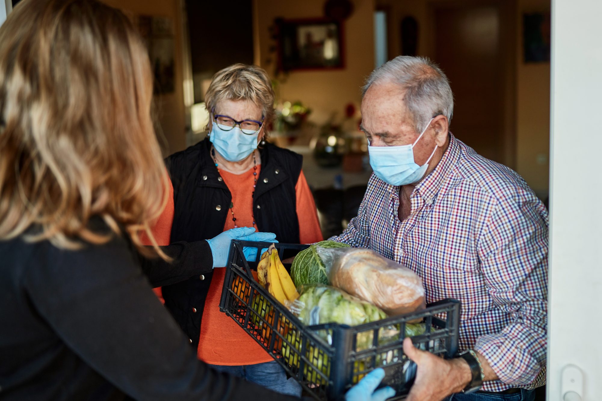 Elderly couple holding a box of food and wearing protective masks.