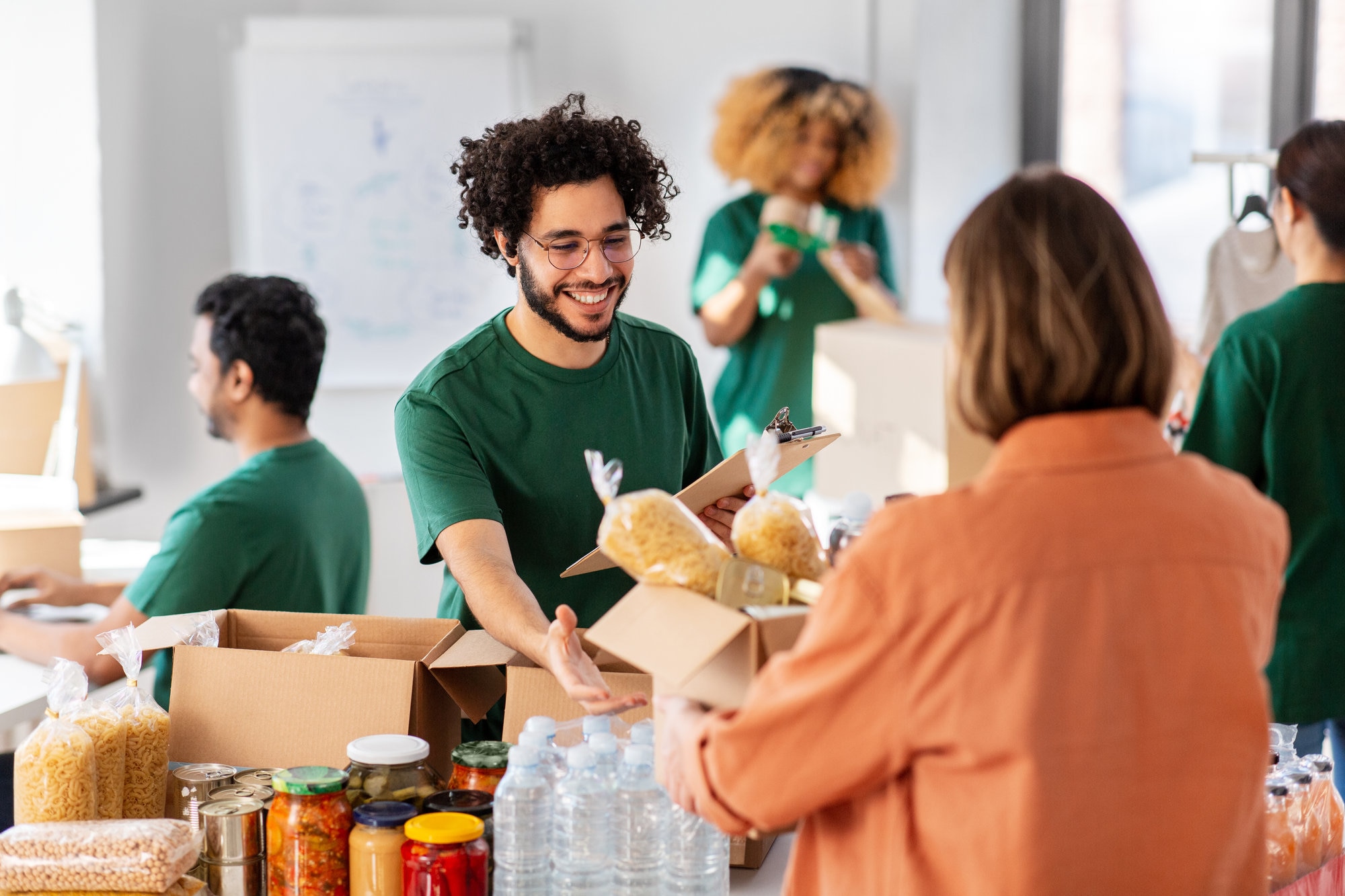A happy smiling male volunteer with a clipboard and a woman taking a box of food at a distribution or refugee assistance center