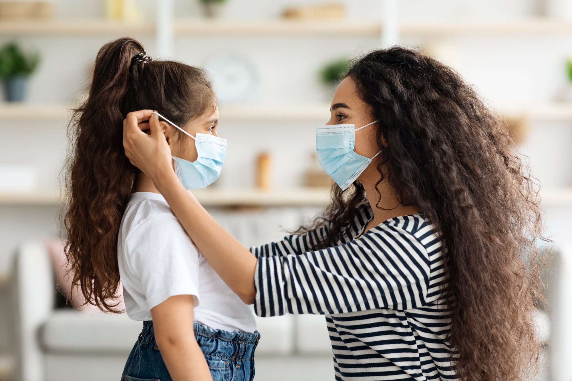 Woman helping a little girl put on her face mask