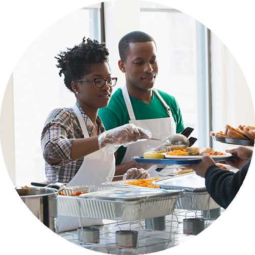 Two people serving food at a soup kitchen represent giving to the Human Services sector.