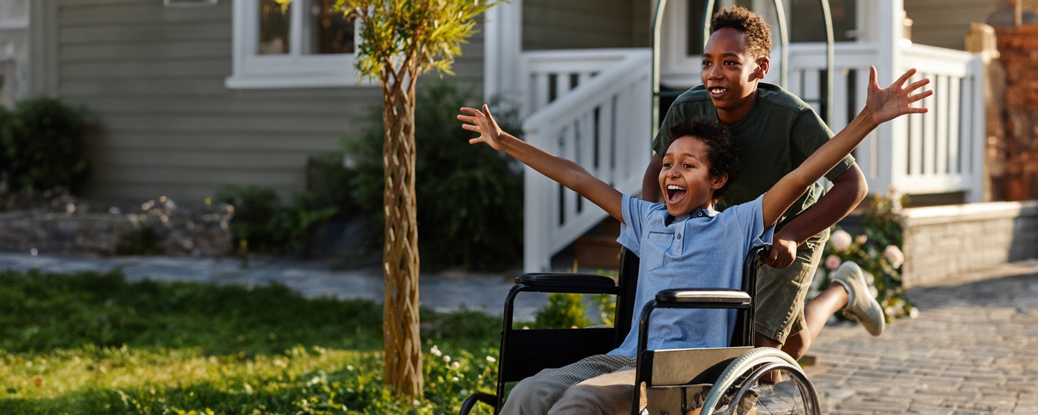 Boy pushing happy boy in wheelchair.