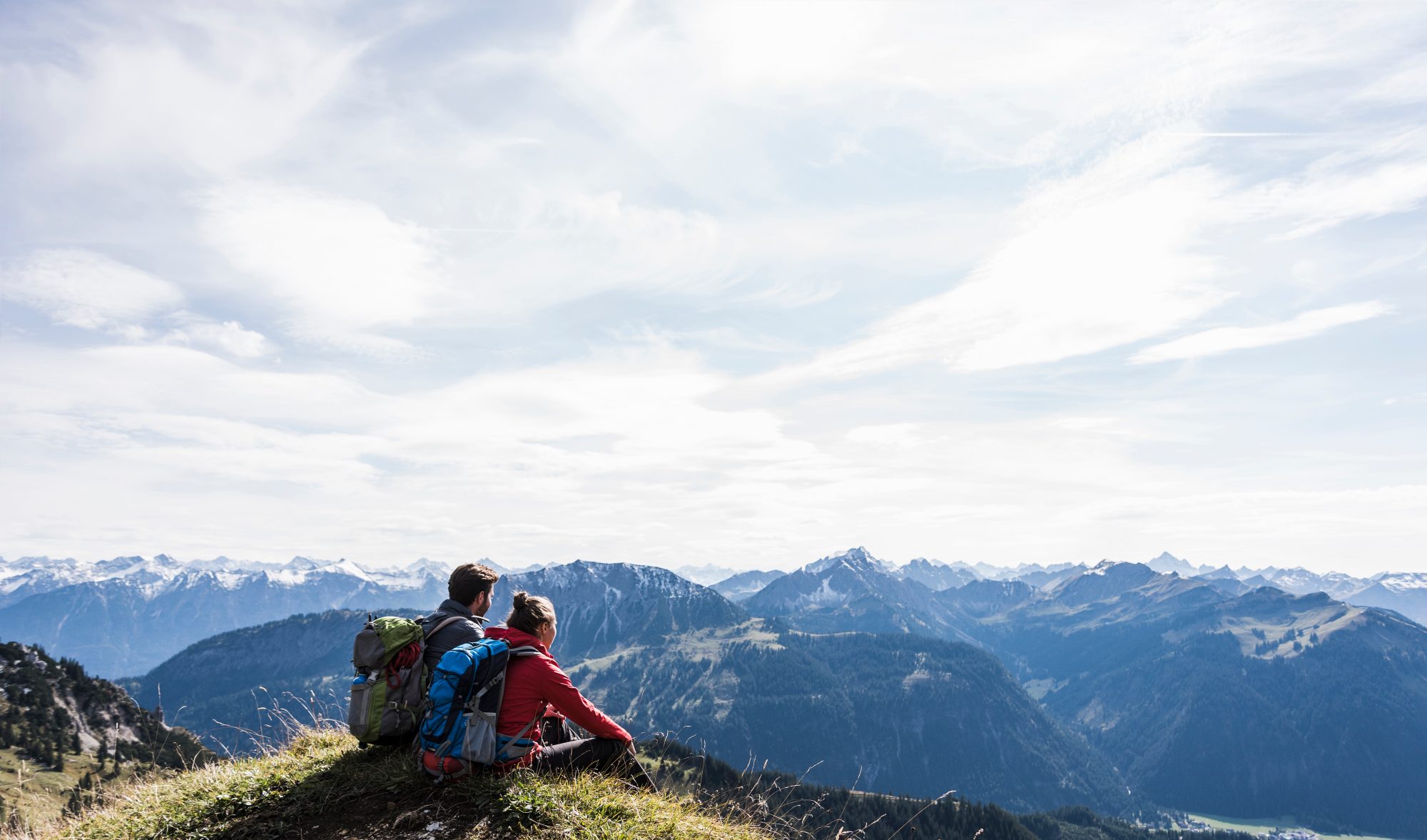 a couple sitting side by side on top of a mountain with a view of a mountain range